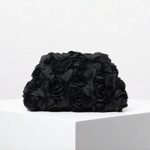 Svart kuvertväska med rosor  - Unik svart kuvertväska täckt av stora, tredimensionella rosor. Väskan har en mjuk form och stängs med guldfärgade detaljer. Perfekt för dig som vill sticka ut med en romantisk och cool accessoar.