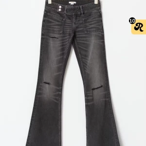 Bootcut svarta jeans  - Svarta bootcut jeans med coola slitningar på benen och framfickor med dubbla knappar i midjan. Jeansen har en snygg tvättad look och är tillverkade i stretchigt denim som sitter skönt. Perfekt för dig som gillar en retro vibe och vill sticka ut.