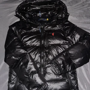 Svart pufferjacka från Polo Ralph Lauren - Helt ny oanvänt Ralph lauren jacka, endast testat en gång och ej kommit fram till någon användning. Luvan går av med hjälp av dragkedja, den är size S passar dessutom M. Inga märken, defects, flöden eller sådana skador.