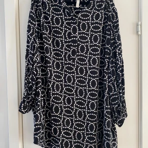 Svartvit mönstrad klänning H&M - Svart kortklänning från H&M med vitt prickigt mönster i cirklar. Klänningen har långärmade ärmar med lätt puff och knappar framtill. Materialet är mjukt och lätt, perfekt för dig som gillar en loose fit och coolt grafiskt uttryck. Mått Över bröstet: ca 72 cm Längd från axeln och ner: ca 86 cm  100% viskos  Kommer från ett djur och rökfritt hem.