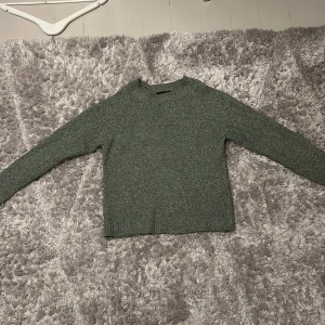 Grön stickad tröja från Vero Moda - Mysig grön stickad tröja från Vero Moda i storlek S. Tröjan har en enkel rund halsringning och långa ärmar. Perfekt för att hålla sig varm och snygg under kyliga dagar. Ribbad kant vid ärmslut och nederkant för extra komfort.