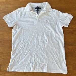 Vit pikétröja Tommy Hilfiger M - Vit pikétröja från Tommy Hilfiger i slim fit stretch-modell. Klassisk krage, knappar framtill och broderad logga på bröstet. Tillverkad i bomull och perfekt för en clean och stilren look.