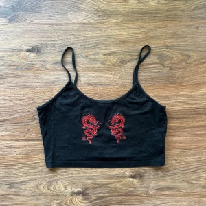 Crop top - Svart croppad linnetopp med tunna axelband och två röda broderade drakar framtill. Snygg och edgy design som sticker ut, perfekt för dig som gillar asiatiska influenser och streetstyle. Materialet känns mjukt och lätt mot huden. Tyget och banden är ganska utsträckta så att den kan sitta lite löst🙃