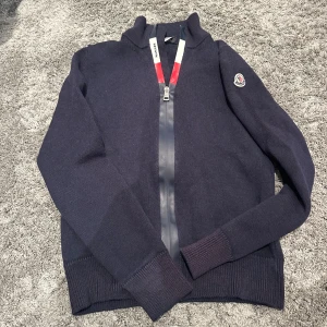 Moncler cardigan - Mörkblå cardigan från Moncler med hög krage och hel dragkedja framtill. Klassisk Moncler-logga på ärmen och snygga ribbade muddar. Ny pris 4999 storlek (164)