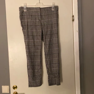 Rutmönstrade kostymbyxor i svart och vitt - Snygga kostymbyxor med klassiskt rutigt mönster i svart och vitt. Byxorna har rak passform och medelhög midja, perfekta för en stilren look. Materialet är mjukt och följsamt, vilket gör dem bekväma att bära hela dagen. Frakt ingår inte 