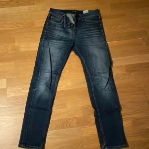 Mörkblå jeans Comfort Mike 30/32 - Snygga mörkblå jeans från Comfort Mike i storlek 30/32. Jeansen har klassisk femficksdesign, raka ben och diskreta slitningar för en cool look. Materialet är jeans med en skön passform och detaljer som kontrastsömmar och läderpatch bak i midjan.