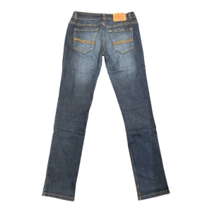 Blå jeansbyxor från Nudie Jeans - Snygga blå jeansbyxor från Nudie Jeans med klassisk femficksdesign och kontrastsömmar. Byxorna har raka ben och subtila slitningar framtill för en cool look. Storleken är okänd då lappen är borta men skulle gissa på W30 | L32! 