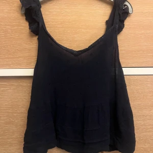 Mörkblå blus med spets från Superdry - Säljer en mörkblå blus från Superdry med volangärmar och spetsdetaljer vid halsringningen. Blusen har ett diskret broderat mönster och är tillverkad i ett lätt, luftigt tyg som ger en skön känsla. Perfekt för dig som gillar romantiska detaljer och en feminin look.