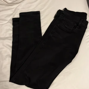 Svarta Replay Anbass jeans - Säljer ett par svarta Replay Anbass jeans med klassisk femficksdesign och snyggt smal passform. Jeansen har en stilren look med svarta sömmar och är tillverkade i ett stretchigt material som sitter skönt hela dagen.