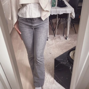 Grå bootcut jeans midrise - Säljer ett par snygga grå jeans med bootcut-modell. Jeansen har klassisk femficksdesign, dragkedja och knapp framtill. Materialet är jeans i en ljusgrå tvätt som ger en fräsch och trendig look. Perfekta för dig som gillar en stilren och avslappnad vibe.