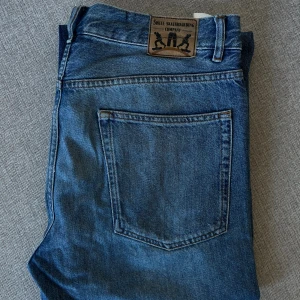 Blå jeans från Sweet Skateboarding - Klassiska blå jeans från Sweet Skateboarding Company med rak passform och normal midja. Jeansen har en enkel bakficka och tydlig logopatch i läderimitation bak i midjan. Tillverkade i slitstarkt denimtyg, perfekta för en avslappnad streetstil. Använt men bra skick! Nypris 600kr size: W33 L33
