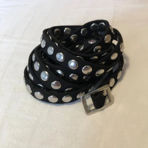 Svart smalt nitarbälte - Svart smalt bälte med nitar längs hela längden. Bältet är mjuk mocka och har en edgy vibe. Längd ca 160cm.