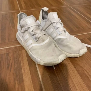 Vita Adidas NMD sneakers - Säljer ett par vita Adidas NMD sneakers med klassiska tre ränder på sidan och snörning. Ovandelen är i mesh och syntet, med detaljer i vitt och ljusbeige på hälen. Skorna har en platt sula och modern streetstil, perfekta för dig som gillar en clean look. Inte slitna bara lite smutsiga. (STORLEK 44 men passar 43 och 42)