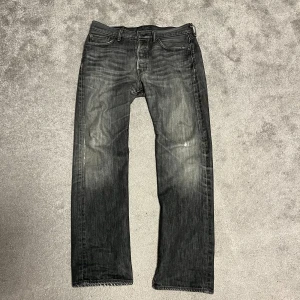 Levi's 501 svarta jeans straight fit - Svarta Levi's 501 jeans med snyggt tvättad look och klassisk femficksdesign. Raka ben och normal passform, tillverkade i slitstarkt jeanstyg. Ikonisk läderpatch bak i midjan och röda Levi's-tag på bakfickan. Perfekta för en avslappnad streetstil.