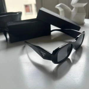 Prada Solglasögon  - Säljer Prada solglasögon, fick de som en gåva men använder dem inte längre, de sitter bara och samlar damm. Säljer dem för 900kr. Det som ingår är originallådan, glasögonduk glasögonfodral, certifikat, och en liten informationsbok.