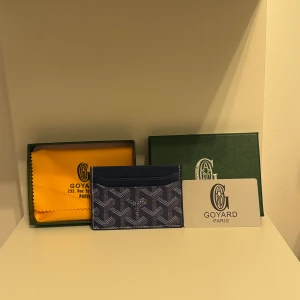 Blå G yard plånbok med mönster - Snygg blå plånbok från G med deras ikoniska grafiska mönster i vitt och grått. Plånboken är tunn och smidig, perfekt för kort och sedlar. Kommer med original ask och tygpåse. Lyxig och stilren accessoar 