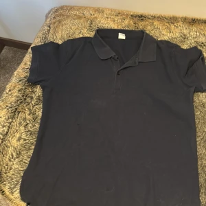 Mörkblå piké med krage - En stilren mörkblå pikétröja med klassisk krage och knappar framtill. Tröjan har korta ärmar och är tillverkad i mjukt bomullsmaterial, perfekt för en avslappnad och snygg look.