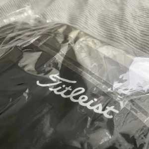 Svart Titleist jacka S - Svart jacka från Titleist med vit logga på bröstet. Perfekt för dig som gillar sportig och clean stil. Materialet är syntet och designen är enkel och stilren. Helt oanvänd och fortfarande i förpackning, perfekt nu mot golfsäsongen också:)