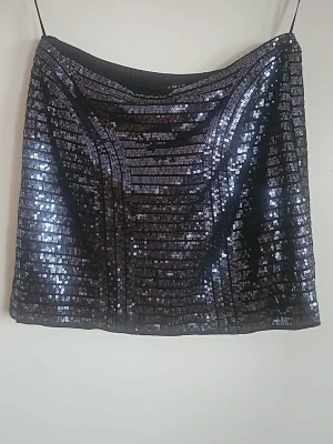 Svart paljettkjol från Amisu - Glittrig svart kortkjol från Amisu täckt med paljetter. Kjolen har en rak passform och är perfekt för dig som vill sticka ut med en snygg och festlig look. Materialet är syntet och paljetterna ger ett riktigt coolt intryck.