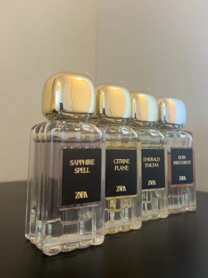 ZARA parfymset med fyra dofter - Fyra exklusiva parfymer från ZARA: Sapphire Spell, Citrine Flame, Emerald Enigma och Ruby Irreverent. Flaskorna är rektangulära i genomskinligt glas med eleganta guldfärgade lock och svarta etiketter. Varje parfym har sin egen färgton på vätskan.