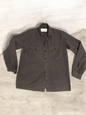  overshirt från A days march - Stilren mörkgrå overshirt från Just Junkies med klassisk krage och två stora bröstfickor med lock och knapp. Rak passform och knäppning framtill. Perfekt lager-på-lager-plagg i mjukt bomullsmaterial.