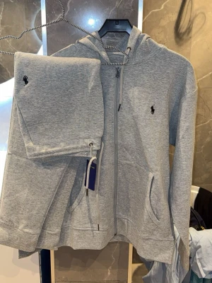   Polo Ralph Lauren - Tracksuit grå size M - Snygga full Tracksuit  från Polo Ralph Lauren med klassisk logga broderad på benet. Byxorna har dragsko i midjan och är gjorda i mjukt bomullsmaterial för maximal komfort. Perfekta för en avslappnad och trendig stil.