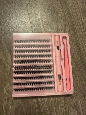 Kit med individuella lösögonfransar - Ett komplett kit med individuella svarta lösögonfransar, pincett och två tuber franslim. Fransarna är i olika längder och har en naturlig böj. Allt levereras i en rosa plastförpackning. Perfekt för att skapa en personlig franslook. Nyskick, PRISET GÅR ATT DISKUTERA!!