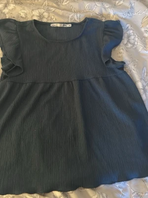 Mörkblå topp med volangärm - Mörkblå blus från Lager 157 med korta volangärmar och rund halsringning. Tillverkad i ett mjukt, lätt och strukturerat tyg som ger en avslappnad känsla. Perfekt att matcha med jeans eller kjol för en trendig look.