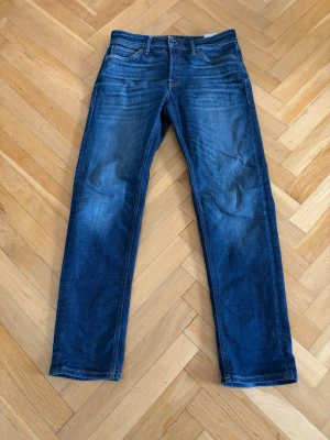 Jeans i färgen blå - Snygga mörkblå jeans med raka ben och klassisk femficksdesign. Jeansen har en lätt tvättad look med subtila slitningar framtill och bakfickor. Perfekta för en avslappnad och stilren stil. Storlek: 30/32