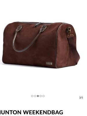 Brun weekendbag i mocka från Vinga sweden - Stilren weekendbag i mörkbrun mocka med detaljer i läder och metall. Väskan har både handtag och avtagbar axelrem, perfekt för resor. Klassisk rektangulär form och diskret logga på framsidan. Jättefint skick. 