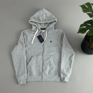 Grå Ralph Lauren Kofta (S) - 🤍 Ralph Lauren kofta – grå 📏 Storlek: S ✨ Skick: Ny med etikett 🎯 Stilren passform, perfekt för en clean look 🤍 Vita snören som ger snygg kontrast 🧵 Mjukt och högkvalitativt material med premiumkänsla 🌟 Klassisk och tidlös Ralph Lauren-design 🛍️ Enkel att matcha till både vardag och mer uppklädda outfits 🎁 Perfekt som present eller garderobsuppgradering 📸 Se bilder för detaljer 