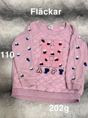 Rosa sweatshirt med H-tryck - Söt rosa sweatshirt från polarn o pyret med stort fluffigt H på bröstet . Tröjan har quiltat mönster framtill och små hjärtformade detaljer i blått, vitt och svart på ärmarna. Ribbstickade muddar vid ärmslut och nederkant.🌸Fläckar. Storlek 110