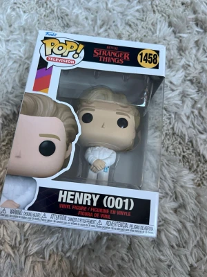 Funko Pop Stranger Things Henry (001) - Säljer en Funko Pop vinylfigur från Stranger Things, modell Henry (001), nummer 1458. Figuren är ljusbeige med blont hår och vit dräkt, och kommer i originalförpackning med fönster. Perfekt för samlare eller fans av serien.
