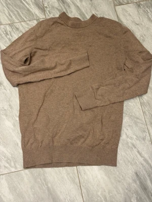 Brun tunnstickad tröja - En enkel och stilren brun tunnstickad tröja med rund halsringning och långa ärmar. Tröjan har ribbade muddar vid ärmslut och nederkant, perfekt för lager på lager och en clean look.