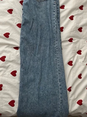 Blå raka jeans från ginatricot  - Säljer ett par klassiska blå jeans från ginatricot med rak passform och hög midja. Jeansen har fem fickor, bälteshällor och stängs med knapp och dragkedja. Tillverkade i slitstark denim, perfekta till en avslappnad look.
