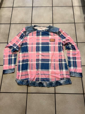 Rutig långärmad tröja med denimdetaljer - Säljer en långärmad tröja med rosa och blått rutmönster. Tröjan har coola denimdetaljer vid axlar, ärmslut och nederkant samt en liten patch framtill. Perfekt för dig som gillar unika plagg med streetkänsla.