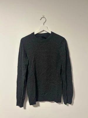 Mörkgrå stickad tröja - Tröjan är från HM och är en  enkel, stilren, mörkgrå, stickad tröja med rund halsringning och långa ärmar. Tröjan har en smal passform och ribbade muddar vid ärmslut och nederkant. Tröjan är knappt använd då jag glömt bort att jag haft den. Pris kan diskuteras. Fler bilder kan skickas vid behov.