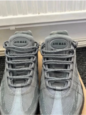 Grå Nike Air Max 95  - Nike Air Max 95 sneakers i helgrå färg med mesh och syntetpaneler. Skorna har tydlig Air Max-dämpning i sulan, snörning framtill och diskreta Air Max-loggor längs sidan. Swoosh-logga på hälen och klassisk rund tå. Perfekt för dig som gillar sportig och clean stil.