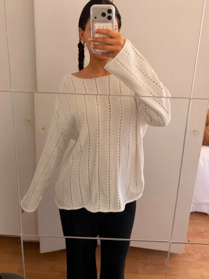 Vit stickad tröja med hålmönster - Säljer en vit stickad tröja med diskret hålmönster i vertikala rader. Tröjan har en avslappnad passform, man kan ha den offshoulder och har långa utsvängda  ärmar. Funkar perfekt som en pullover över en bikini under sommaren oxå! 