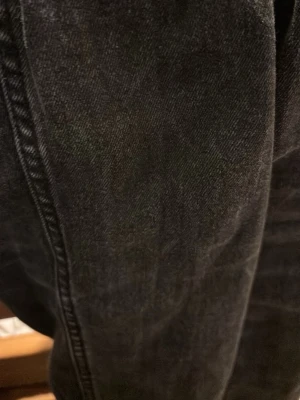 Byxor - Säljer ett par svarta jeans med rak passform. Jeansen har klassiska sömmar och är tillverkade i denim. Perfekta för en avslappnad och stilren look.