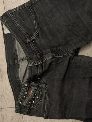 Svarta Lågmidjade jeans med nitar från Diesel - Säljer ett par Snygga svarta jeans från diesel med typ rak passform och coola nitar på myntfickan. De är väldigt Lågmidjade Jeansen har klassisk femficksdesign och gylf. Är strl w31 men skulle säga att de passar en M. Säljer pga ej min strl 🫶🏼