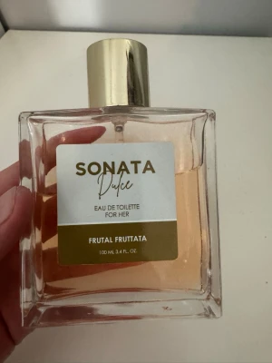 Sonata Dulce Eau de Toilette 100ml - Fräsch och fruktig parfym för henne från Sonata, modell Dulce Frutal Fruttata. Kommer i en stilren, fyrkantig glasflaska med guldig kork och ljusrosa vätska. Perfekt för dig som gillar söta och fruktiga dofter.