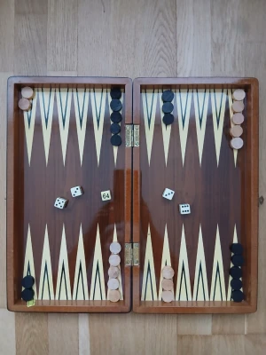 Backgammon- och schackbräde i trä  - Snyggt spelset i trä med backgammon på insidan och schackbräde på utsidan. Inkluderar spelpjäser i svart och beige, tärningar och dubbleringskub. Perfekt för spelkvällar med vänner eller familj. Mått : 38 x 41 cm.    OBS! “Det finns en mindre defekt (se bild).”