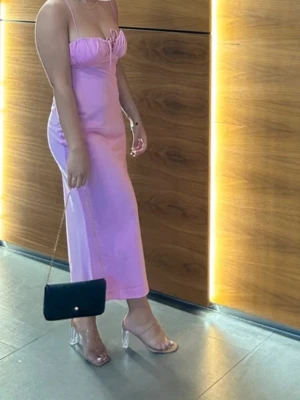Ljuslila långklänning med smala axelband - Snygg ljuslila långklänning med smala axelband och figurnära passform. Klänningen har en enkel och stilren design med lätt rynkdetalj vid bysten. Perfekt för dig som vill ha en feminin och trendig look.