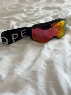 Spegelglasade skidglasögon med svart band - Säljer ett par snygga skidglasögon från EQPE (barn) med spegelglas i rött och gult. De har ett svart elastiskt band med vit logga och en modern, sportig design. Perfekta för dig som vill sticka ut i backen!