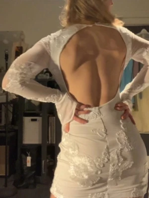 Vit blommig kortklänning med öppen rygg - Supersnygg vit kortklänning med stora blommiga broderier och transparenta långa ärmar. Klänningen har en öppen rygg och utsvängda ärmslut. Köpt från Plick men säljer vidare då jag hittat en annan klänning till studenten och denna inte kommer till användning. Jättefin klänning!❤️Sista 3 bilder är inte mina 
