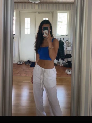 Vita linnebyxor med dragsko - Säljer ett par vita linnebyxor med avslappnad passform och dragsko i midjan. Byxorna har raka ben och är tillverkade i ett lätt och luftigt linnematerial. Perfekta för en chill och stilren look. Tyvärr har ena byxbenet fastnat i en cykelkedja, därav de små svarta prickar längst ner på ena benet. Storlek XS