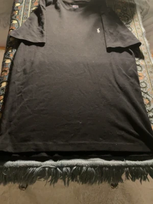 Svart t-shirt från Polo Ralph Lauren - Klassisk svart t-shirt från Polo Ralph Lauren med liten broderad logga på bröstet. T-shirten har rund halsringning och korta ärmar, perfekt för en stilren och enkel look. Tillverkad i mjuk bomull som känns skön mot huden.