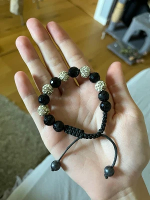 Svart och silver pärlarmband - Fett gulligt armband med svarta facetterade pärlor och glittrande silverfärgade pärlor. Armbandet har justerbar knytning i svart snöre och passar perfekt för dig som gillar en stilren men ändå iögonfallande accessoar.