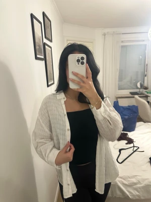 Vit rutig skjorta i bomull - Säljer en vit skjorta med diskret rutigt mönster. Skjortan är långärmad, har knappar framtill och är gjord i ett lätt bomullstyg. Perfekt att bära öppen över ett linne eller stängd för en mer klassisk look.